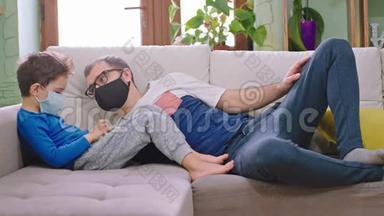 在家里的沙发上，爸爸和他的小儿子在一起，戴着防护面具，他们用智能手机来做防护