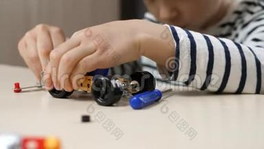 一个小男孩从一个金属建筑套件<strong>中建</strong>造一个汽车模型，扭曲零件：车轮，螺母，螺丝。 孩子`的手