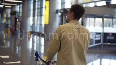 布吕内特，一个穿着米色衬衫的留胡子的人，带着行李手推车在国际机场散步。 匆忙中走着