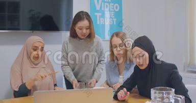 四个自信的、开朗的、多样化的同事办公室女头巾讨论商业计划使用笔记本电脑图表