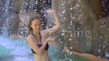 一位年轻女子在热带度假胜地，有温泉、瀑布和游泳池，有热水。 慢动作