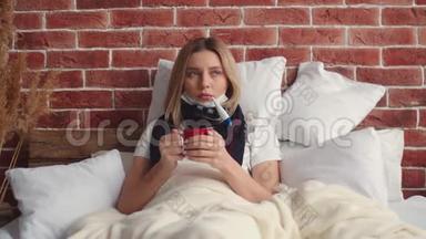 一个戴着围巾的生病的女孩躺在床上喝杯茶，<strong>测量体温</strong>并观察<strong>体温</strong>