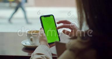 美丽的女人使用手机与绿色触摸屏在咖啡馆。 绿色屏幕。 在社交媒体上分享信息。