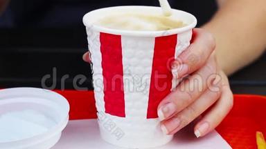 一个女人`手拿着一<strong>杯</strong>卡布奇诺咖啡，用<strong>吸管</strong>搅拌。