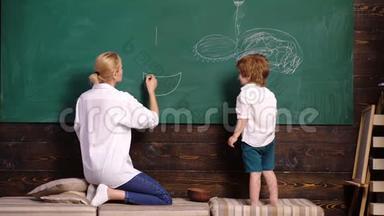 <strong>幼儿</strong>教师和<strong>幼儿</strong>男孩在黑板上作画。 女人和男孩画画。 母亲和儿子用粉笔在