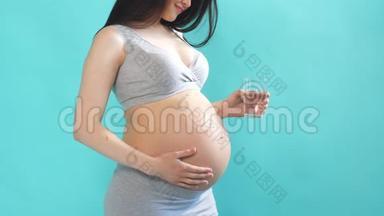 年轻的孕妇从杯子里喝着清爽的水