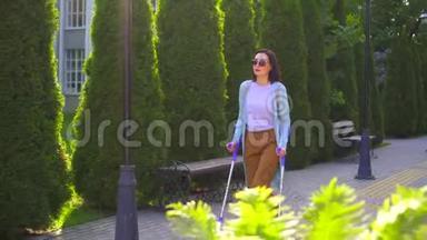 阳光城公园里，一个身体受伤的漂亮年轻女子<strong>拄着拐杖</strong>走路
