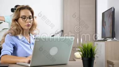 疲惫而<strong>稳重</strong>的女人在电脑上工作，而她的男朋友在后台戴着虚拟现实耳机
