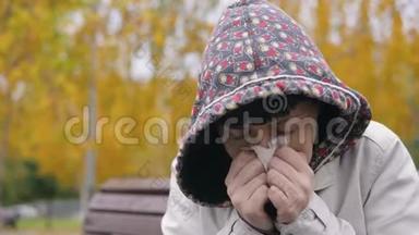一个穿着帽衫的年轻女人在秋天公园打喷嚏和鼻涕。