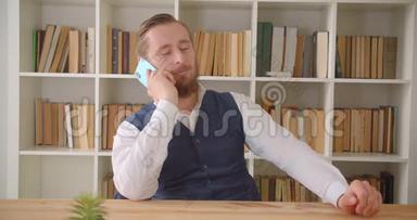 一位年轻的<strong>高加索</strong>商人在办公室打电话的特写镜头，办公室里放着书架