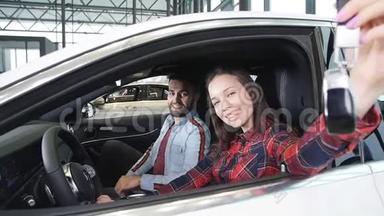 一对年轻幸福的夫妇买了一辆新车。 微笑并显示钥匙