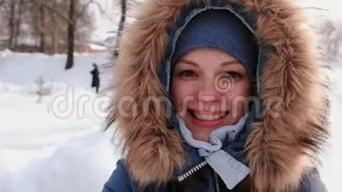 穿着皮衣帽的年轻美女，在雪天的冬季城市公园里与视频连接和行走