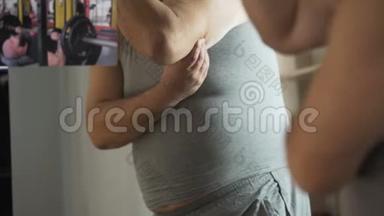 丰满的男人看着照片上肌肉发达的运动员，摸着他肥胖的腹部