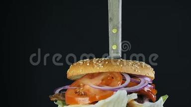 一个多汁的大汉堡，有一个双面包和一个双切片，上面有绿色和蔬菜，用刀子钉在上面