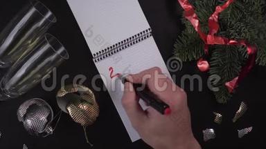 一个年轻人在笔记本上写下了“2020年目标”这几个字，放在一张木桌上，桌上围着圣诞庆典的主题