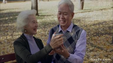 幸福的老年夫妇坐在户外用手机拍照