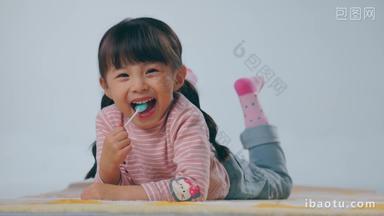 <strong>快乐的</strong>小女孩趴在地毯上吃棒棒糖