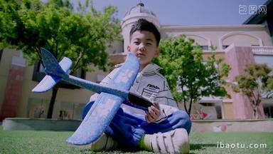 快乐的小男孩坐在草地上玩飞机