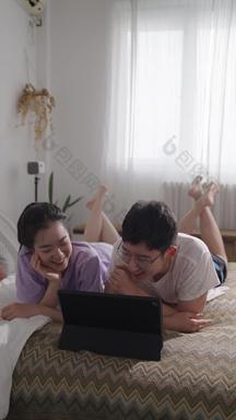 年轻情侣趴在床上使用电脑