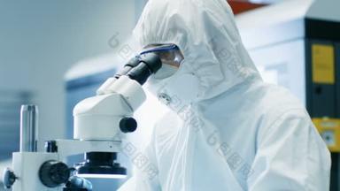 显微镜下的工程师/技术员/科学家检查组件的特写。他在工作项目时穿着无菌工作服和防护眼镜。.