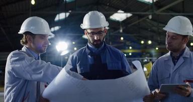 三位戴头盔的工程师用平板电脑和大纸图纸拍摄的肖像照片, 讨论他们的新工作项目。在一个大工厂里.