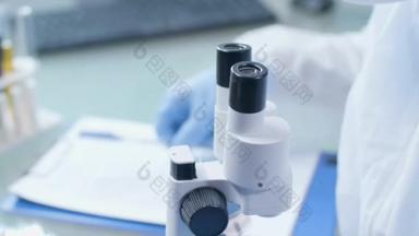近距离拍摄实验室技术人员在观察显微镜时做笔记