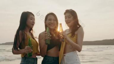 一群亚洲少女在沙滩上聚会庆祝，晚上日落时，朋友们在沙滩上愉快地喝啤酒。户外旅游假期假期夏季概念。慢动作拍摄.