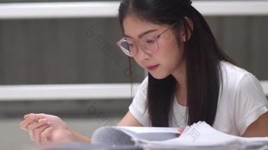 亚洲学生妇女读图书馆的书籍在大学。年轻的本科生女孩做家庭作业，读课本，努力学习知识和教育在课桌在大学校园的概念.