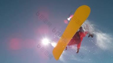 慢动作特写：滑雪者跳大的空气踢<strong>腿</strong>，喷洒雪花，在完美的冬日飞越太阳。 滑雪板在雪地公园里跳跃. 阳<strong>光</strong>从高山上的跳板上照射过去