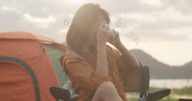 年轻的亚洲露营者夫妇使用相机在海滩附近互相<strong>拍照</strong>。男人和女人在黄昏的浪漫时刻快乐地<strong>旅行</strong>.户外活动、探险<strong>旅行</strong>或度假.