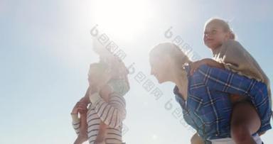 一对白种人夫妇带着他们的儿子和女儿一起在海滩上享受闲暇时光的低角度侧视图，他们带着孩子们缓慢地坐上大海和蓝天的背风