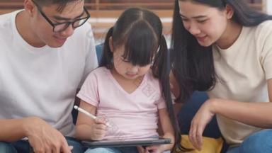 快乐的亚洲家庭爸爸，妈妈和女儿在客厅里用电脑平板技术坐在沙发上。自我隔离、待在家里、与他人保持距离、检疫以预防结肠炎.
