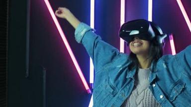 快乐的年轻女人环顾四周，想知道在VR耳机里有多神奇。彩灯背景下的虚拟现实头盔