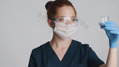 带防护眼镜、面罩和医用手套的专业女医生，与隔离的烧瓶一起工作