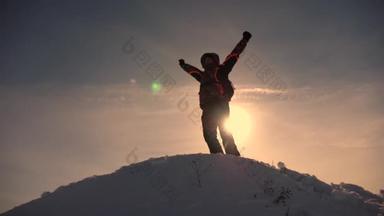 旅行者爬上山顶，为胜利感到高兴，挥挥手，沐浴在阳光中。登山者冬季登山之旅.旅行者爬上山顶.爬山者徒步旅行.