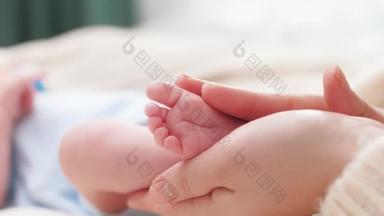小婴儿的脚在女性的手中。年轻的母亲轻轻地触摸和抚摸她新生的小腿。家庭幸福和有年幼子女的慈爱父母的概念.