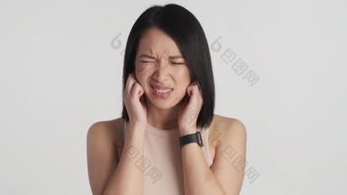 年轻的亚洲女人用手指捂住耳朵，远离白色背景的噪音。这么大声的表达。什么都不想听