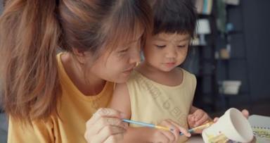 <strong>快乐快乐</strong>的亚洲家庭妈妈教蹒跚学步的小女孩画瓷壶在客厅的桌上玩乐放松。在一起度<strong>过</strong>的时间、社会距离、检疫以预防结肠炎.