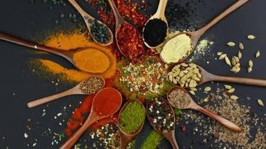 Dry colorful spices in spoons and bowls with fresh seasoning on dark background, top view
