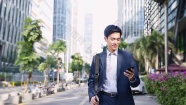 在现代城市，年轻的亚洲商人一边走在大街上一边<strong>看手机</strong>