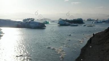 浮在水面上的冰块。阳光下的景色。飞越靠岸的人们，观看令人惊奇的自然景观。冰岛