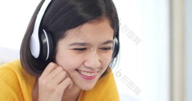 笑着的年轻亚洲女人的画像是躺在床上用耳机听音乐。在家里观看视频娱乐的亚洲女孩的近视
