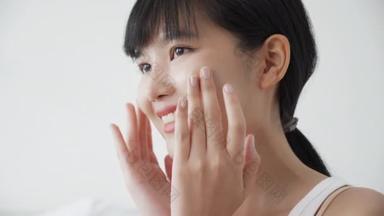 美丽的年轻亚洲女人喜欢在脸上涂上润肤霜或润肤乳液，漂亮的亚洲女人喜欢用化妆品、<strong>护肤</strong>和健康观念来触摸皮肤.
