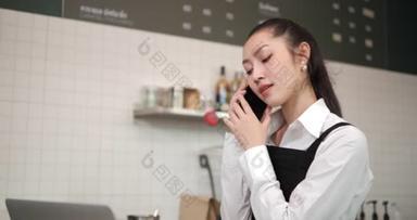 在咖啡店工作的亚洲妇女咖啡店员工。微笑的女服务员收银员在电话上向顾客订<strong>购</strong>咖啡和烘焙面包。小<strong>企业</strong>主和非全日制工作概念