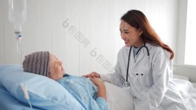 有爱心的亚洲医生在医院病床上看望老年妇女病人，友好的医生牵着病人的手与她交谈，感到好消息。老年人保健概念.