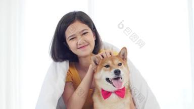 与志巴依努<strong>宠物</strong>狗在床上休息时看着相机的快乐微笑的女人的画像.
