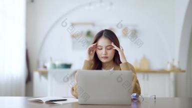 办公室综合症的概念。过度劳累的年轻亚洲女人感到头疼，电脑笔记本电脑工作后视力出现问题。在家里疲惫不堪的紧张的成年女商人