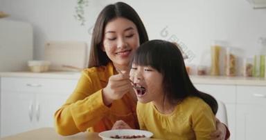 早上在家里的例行公事可爱可爱的亚裔母亲坐在<strong>厨房</strong>里，用牛奶和麦片喂女儿