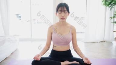 从一个在瑜伽垫上练习瑜伽、做阿达哈 · 帕迪亚马纳纳运动、半莲花式冥想、在家锻炼、穿运动服的亚洲女运动员身上变焦。4k慢动作视频.