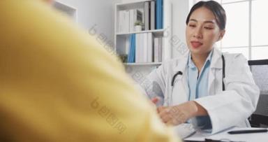 身穿白衣的年轻亚洲女医生在诊所或医院办公室的办公桌前讨论触摸女病人肩膀的问题。心理帮助概念.